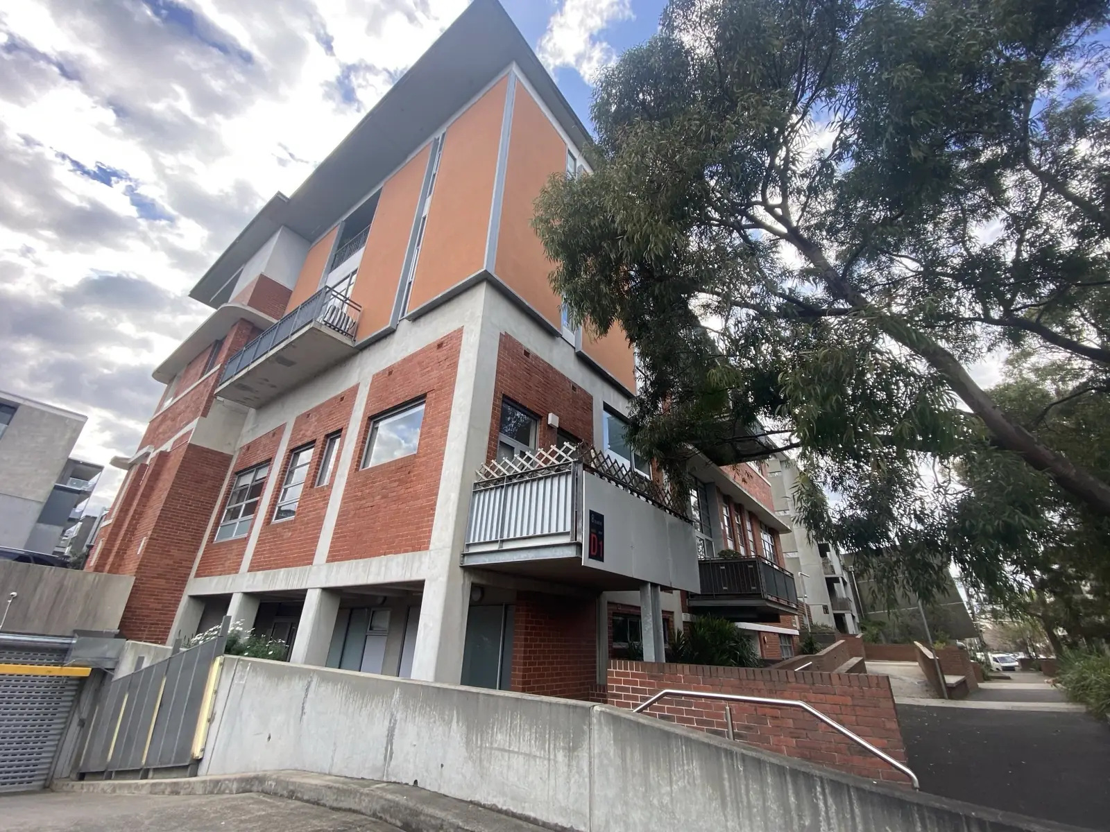 Brick apartment building with stacked balconies beside a mature tree