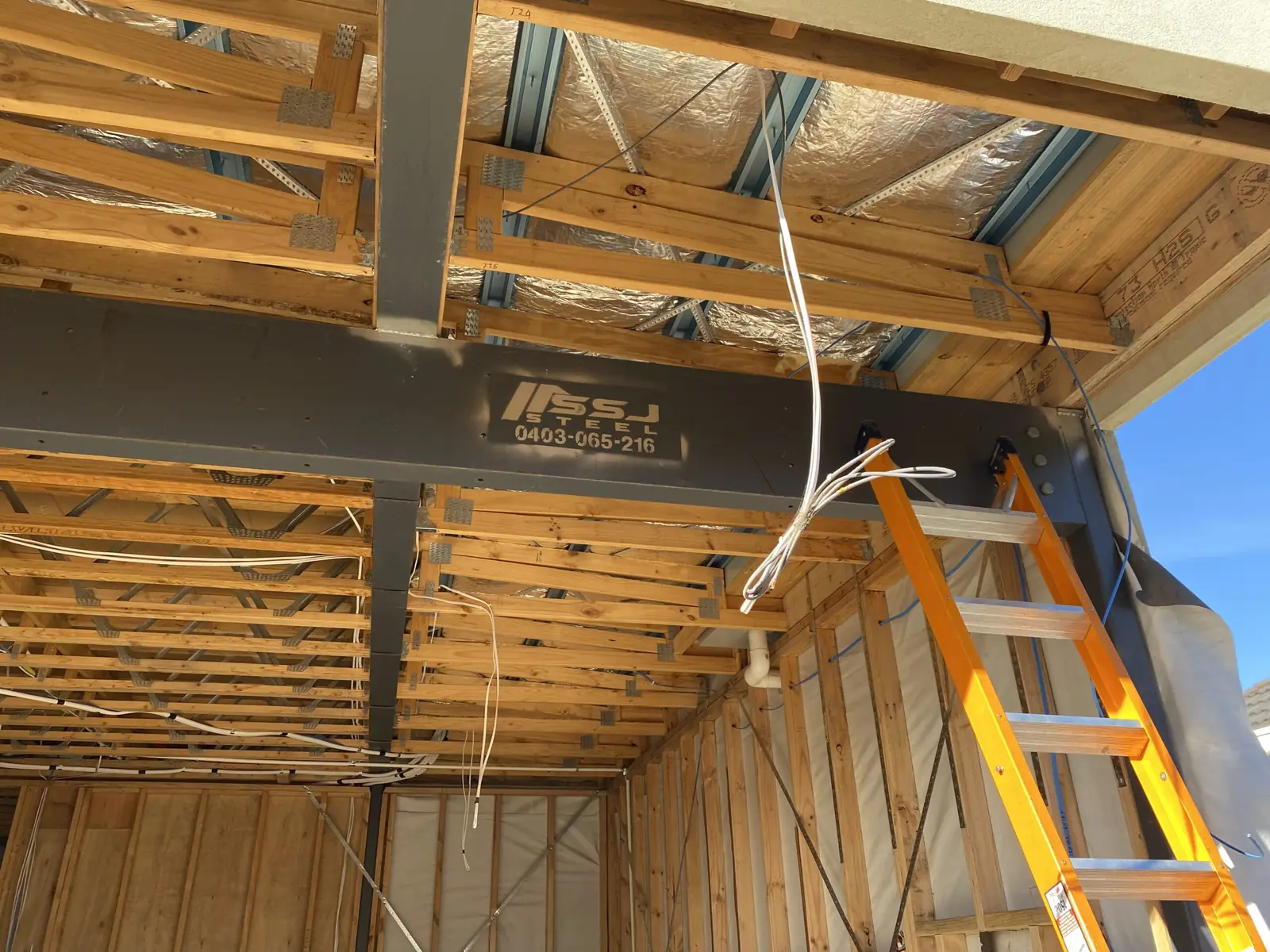 Interior of a building under construction — exposed timber framing, foil insulation and a ladder against the wall