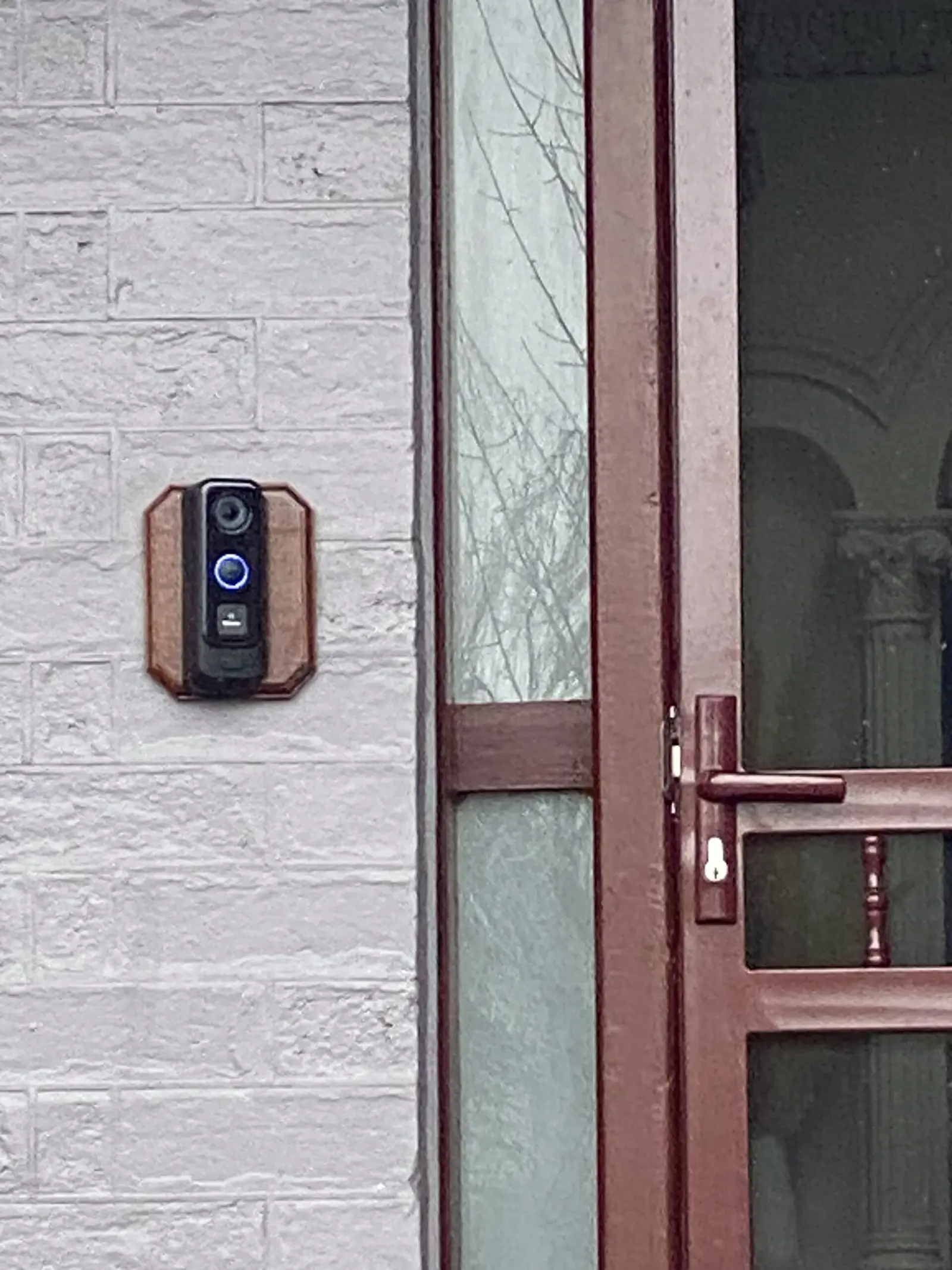 Intercom panel mounted on a brick wall beside a glazed entry door