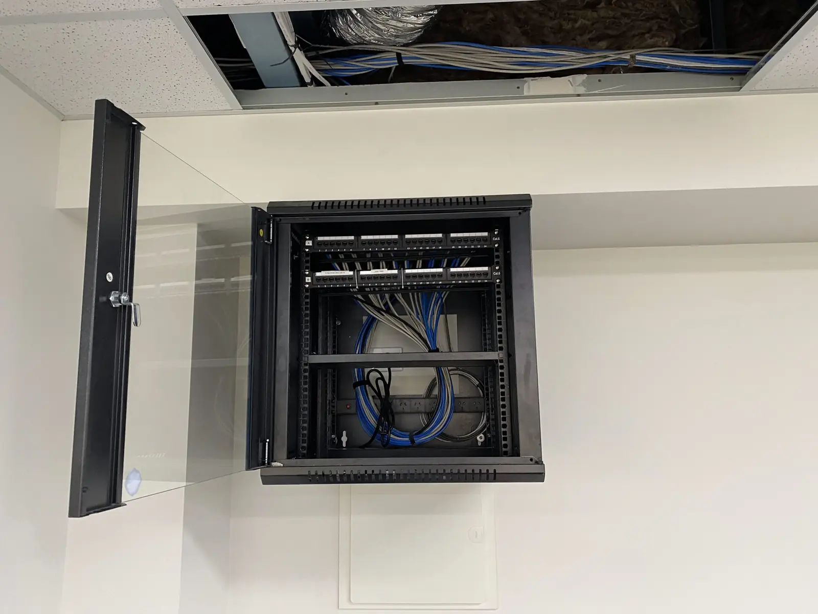 Open comms cabinet with blue cabling running up into the ceiling void above