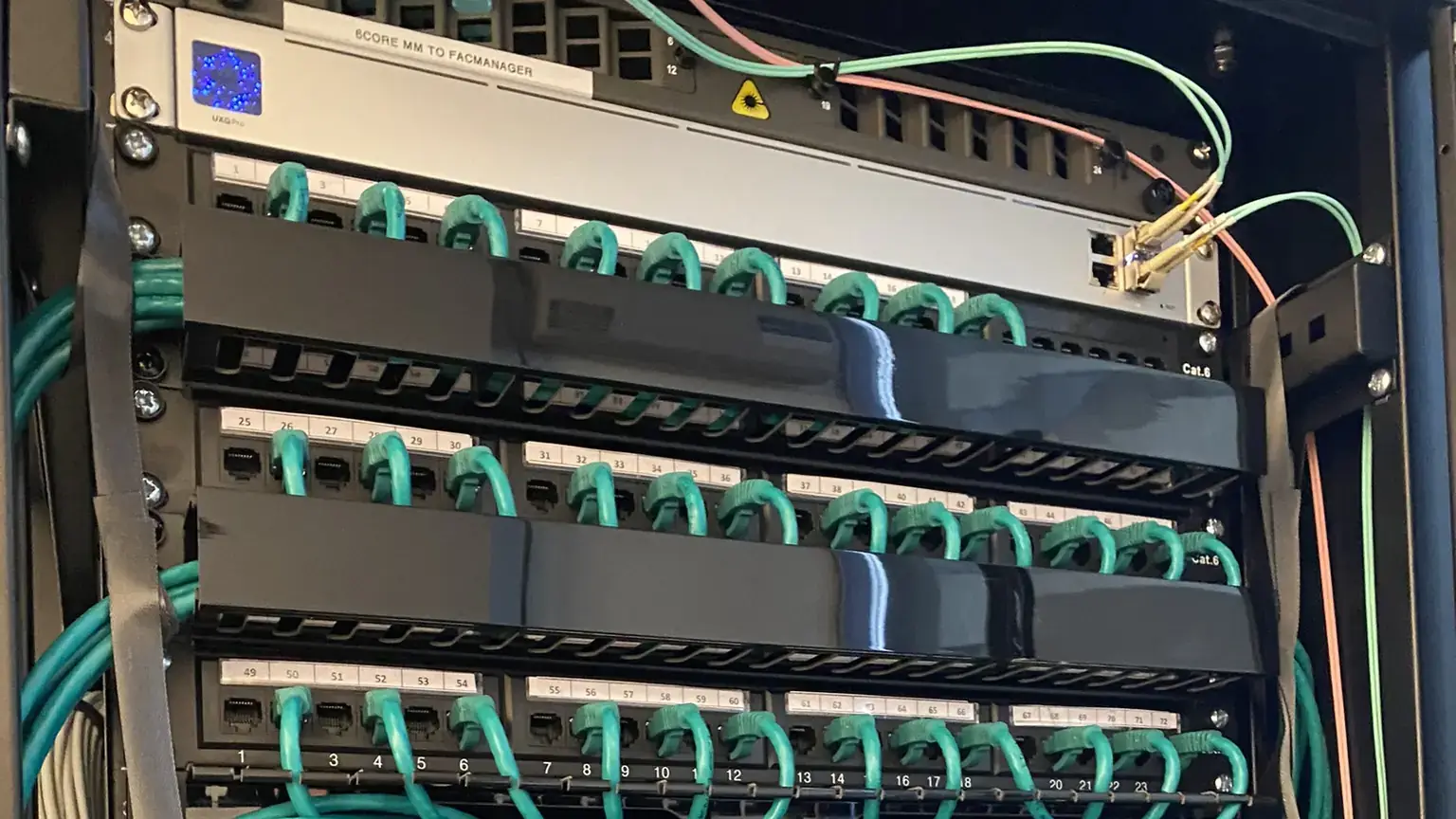 Numbered Cat6 patch panels with teal leads dressed in even loops down into the switch below