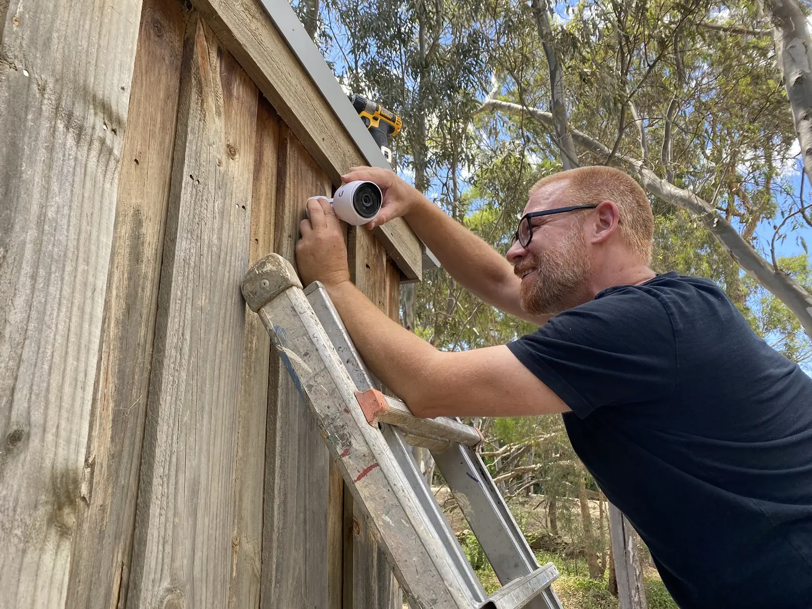 Technician on a ladder fixing a camera bracket to a timber fence