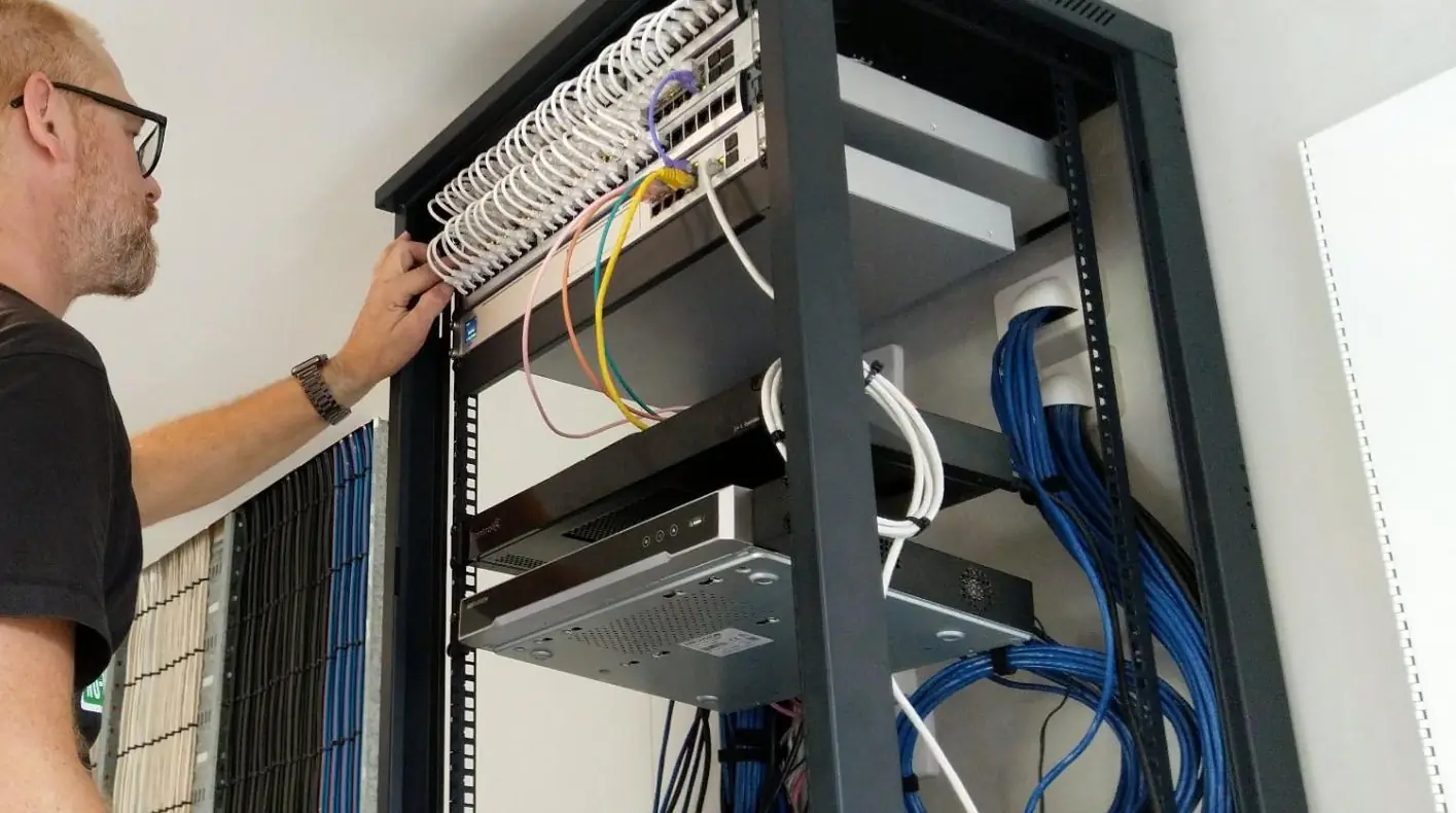 Technician working inside an open wall-mounted rack, dressing network cabling into a patch panel