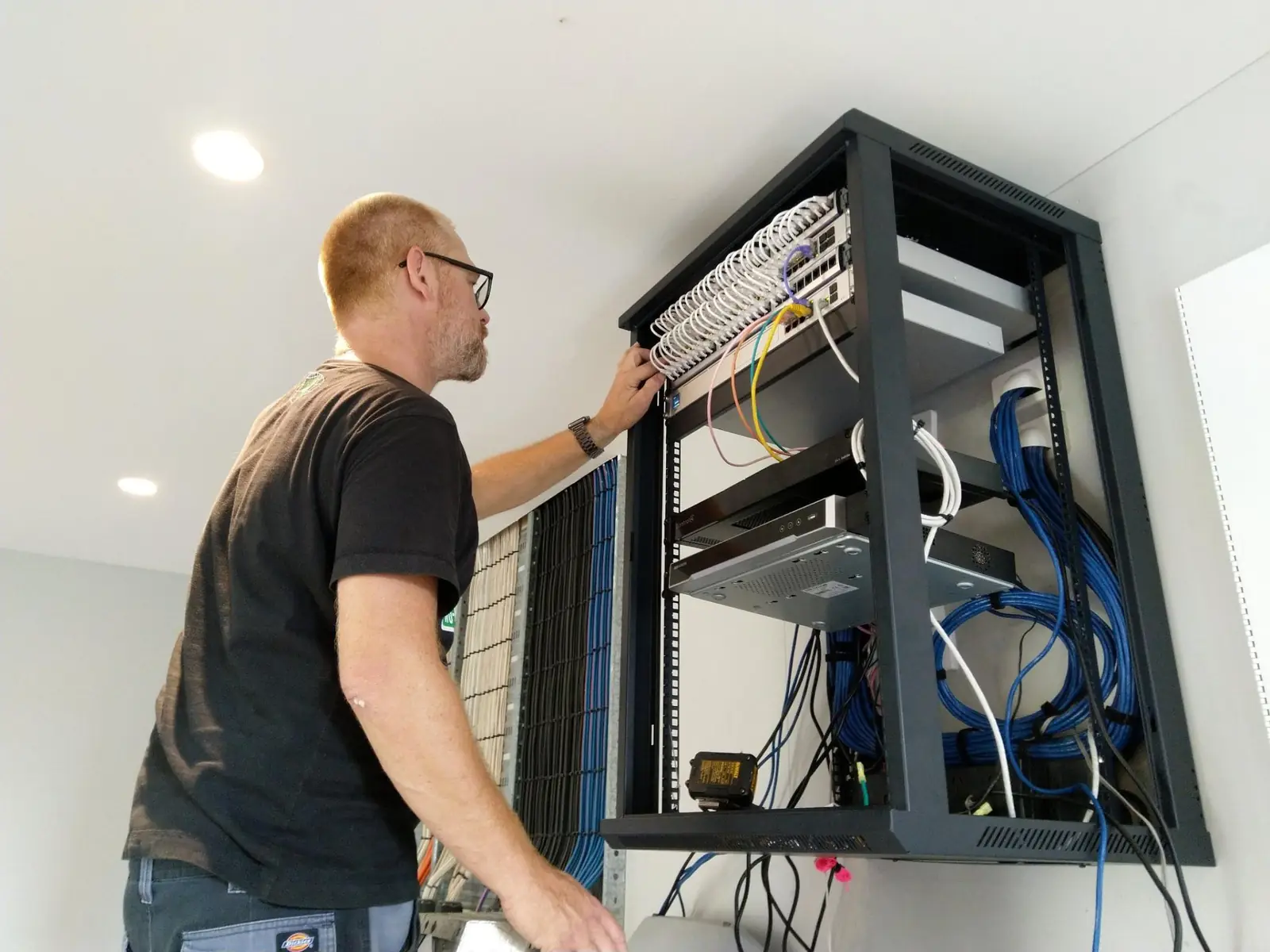 Technician dressing network cabling into a patch panel inside an open wall rack