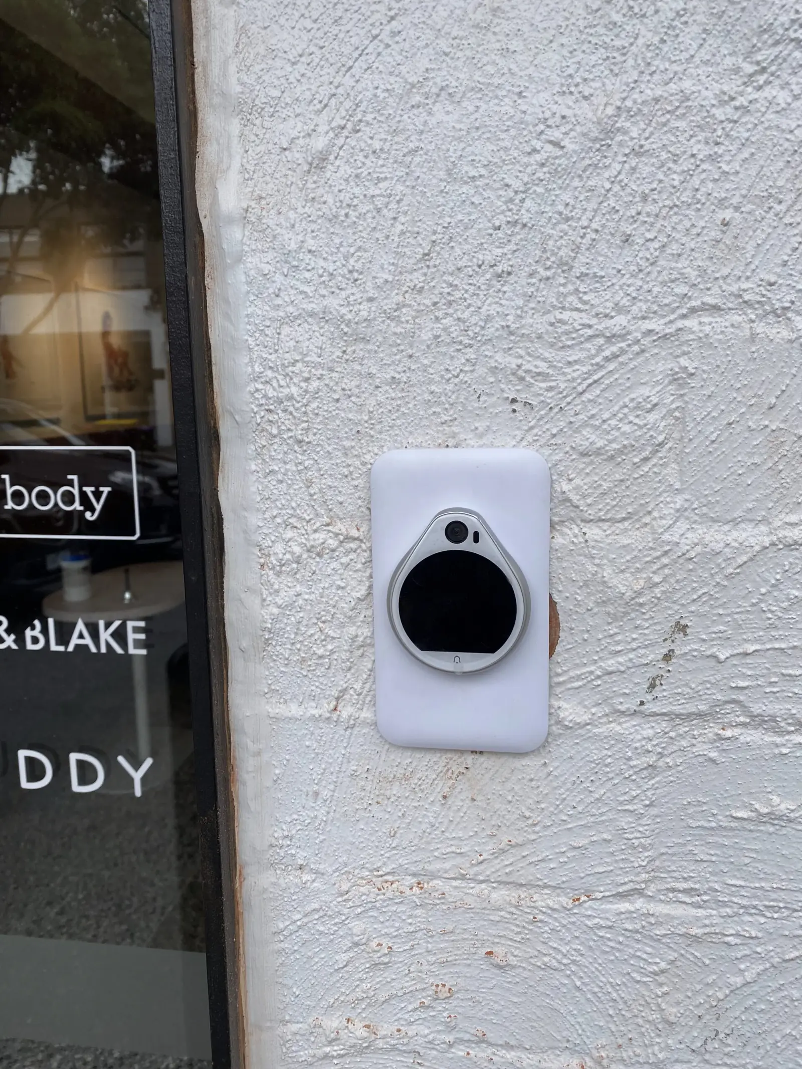 Video intercom panel mounted beside a shopfront window on a rendered wall