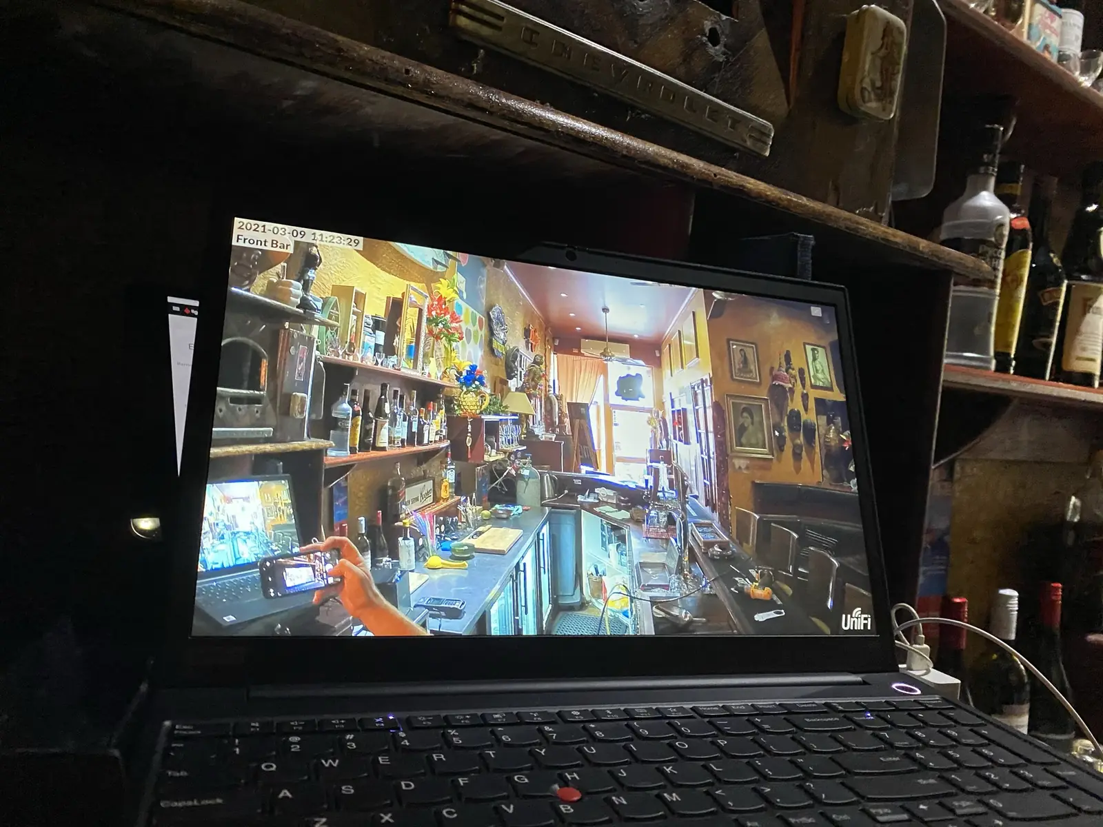 Laptop on a bar bench showing the live camera view of the venue behind it