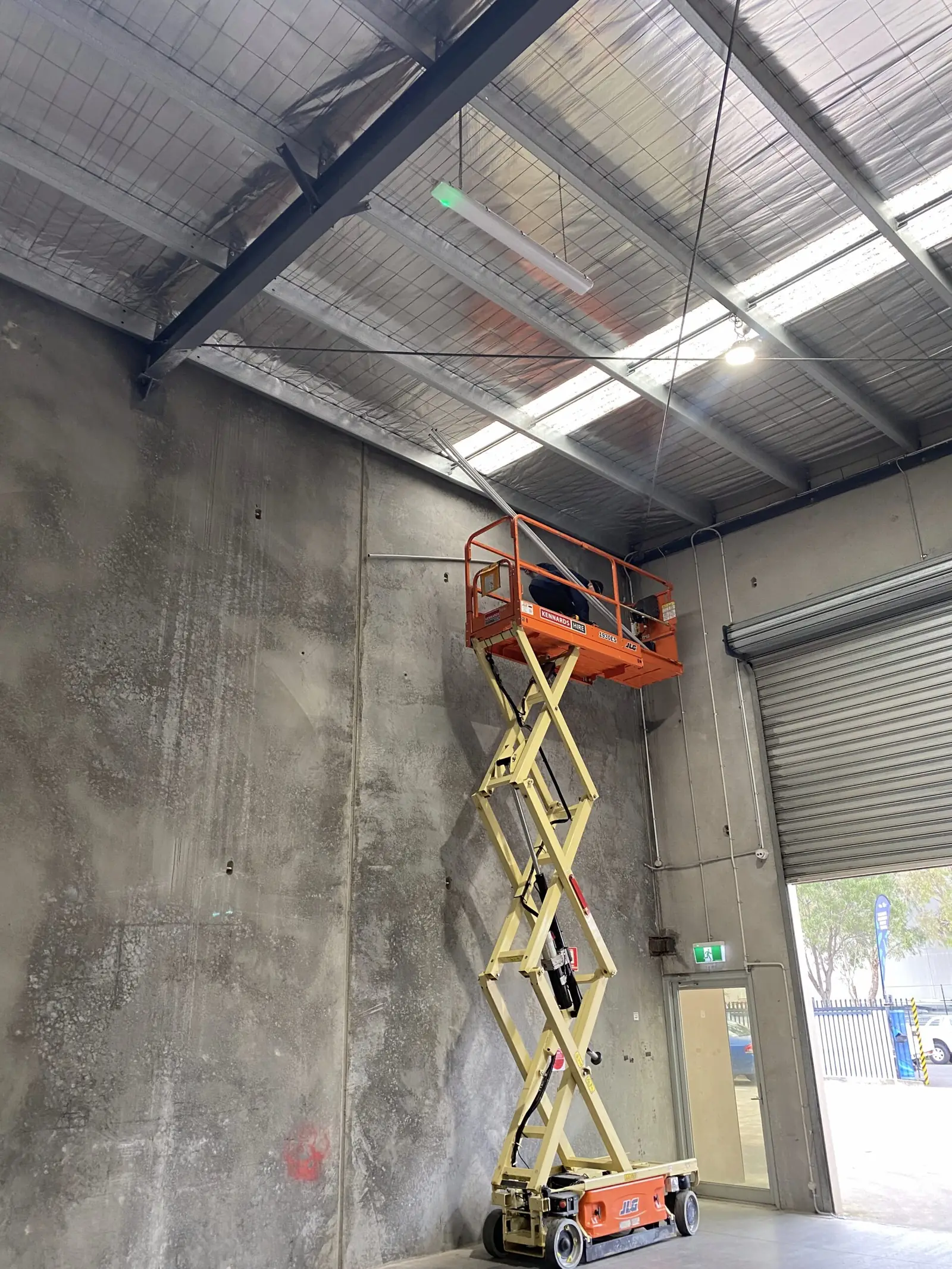 Warehouse interior with a scissor lift positioned near a roller door and high steel ceiling