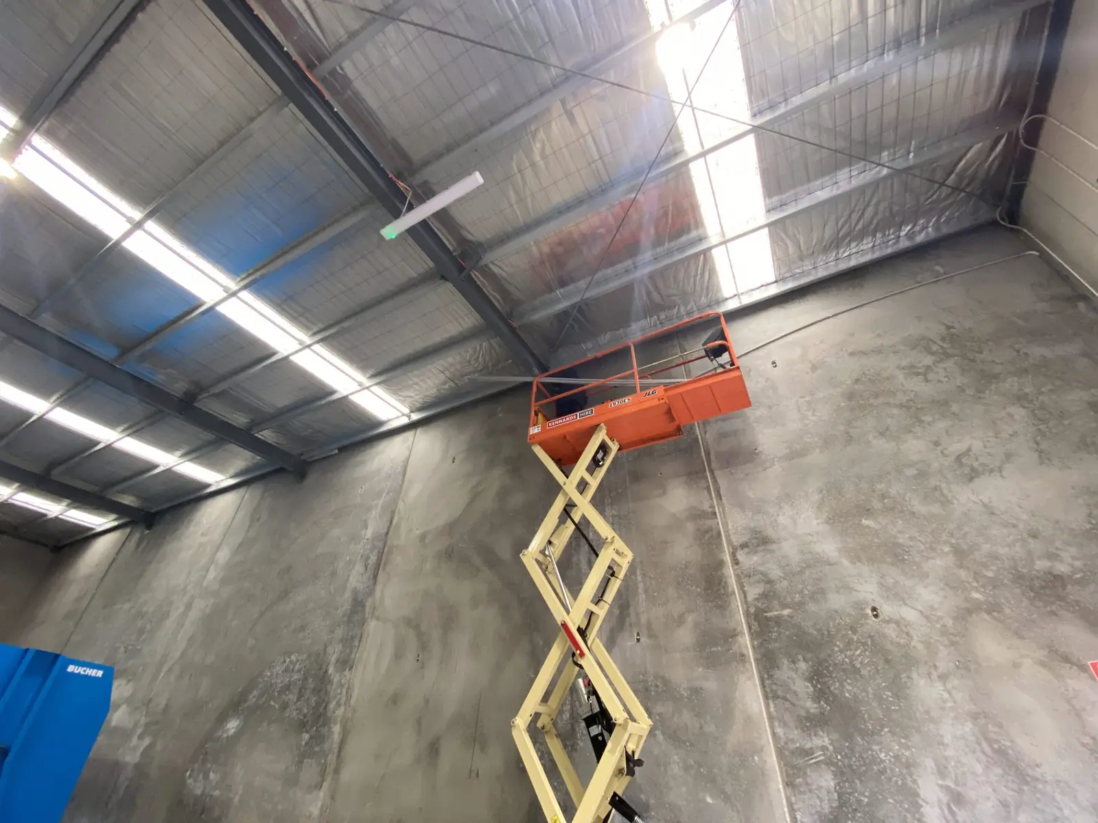 Scissor lift raised toward the steel roof structure of a warehouse